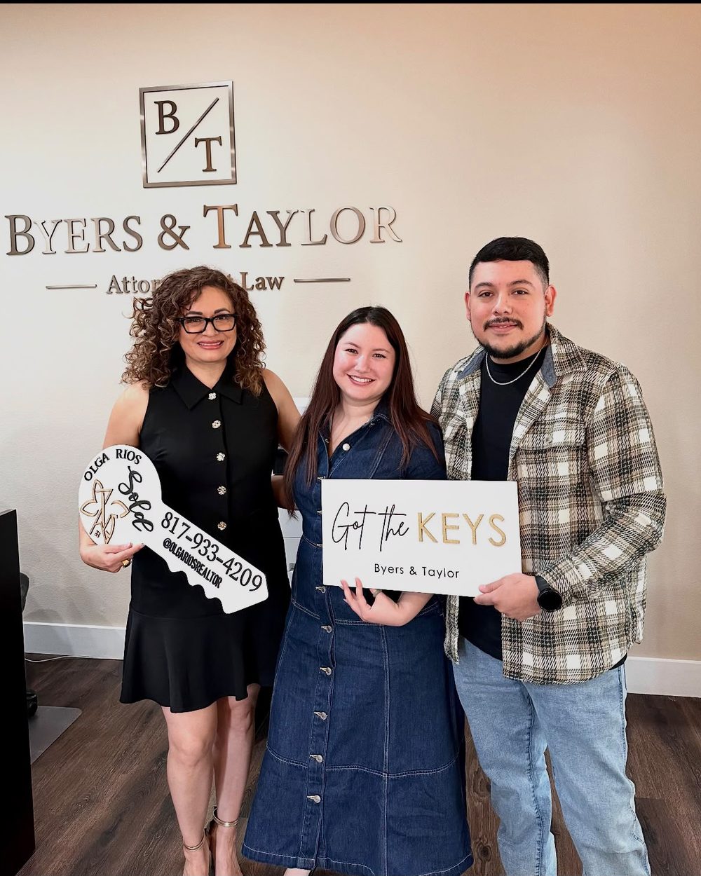 A couple holding a Got the Keys sign with their agent on closing day