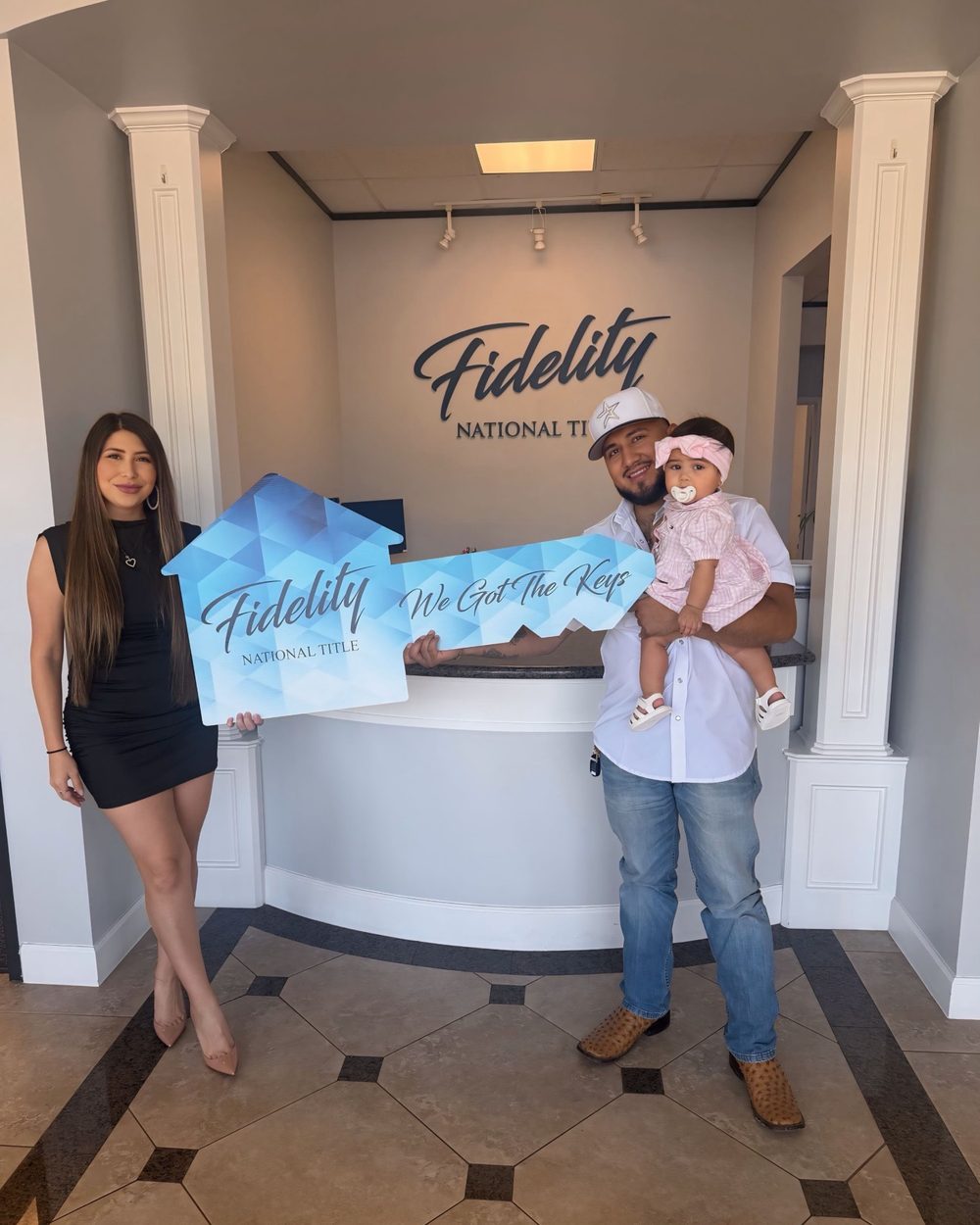 A couple with their baby holding a We Got the Keys key at the title company