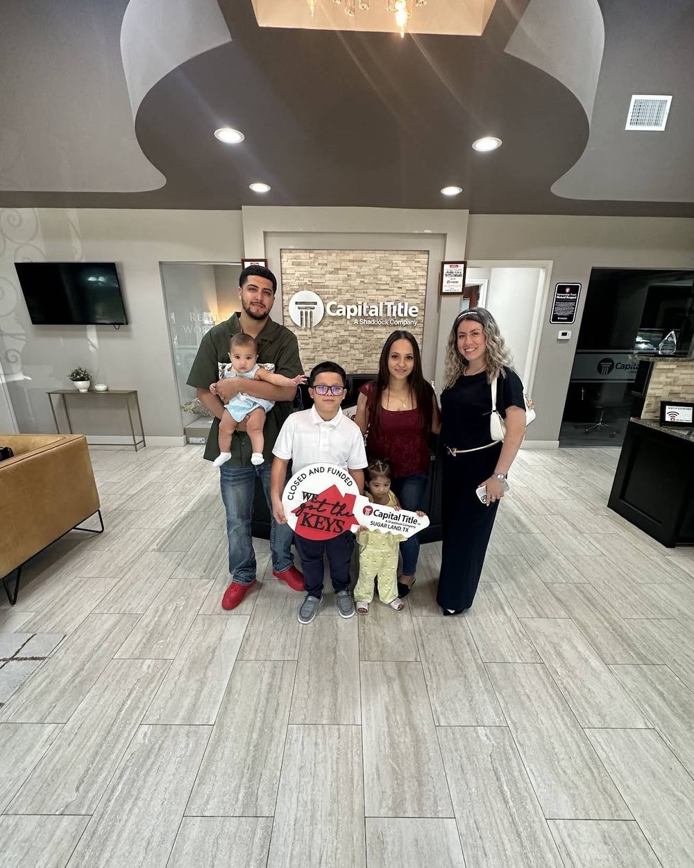 A family with young children holding a Capital Title We Got The Keys sign