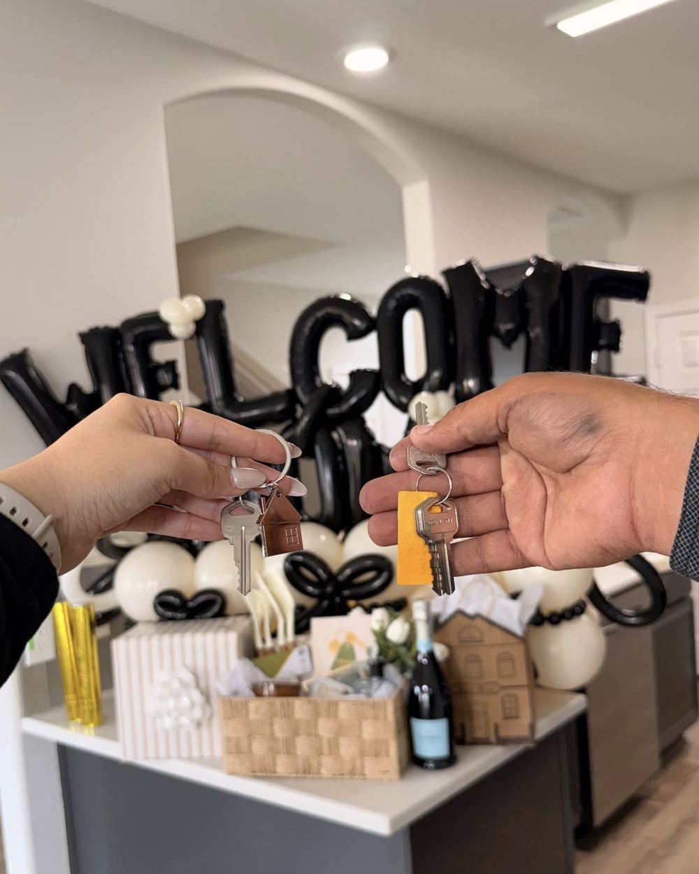Two hands holding house keys in front of Welcome balloons