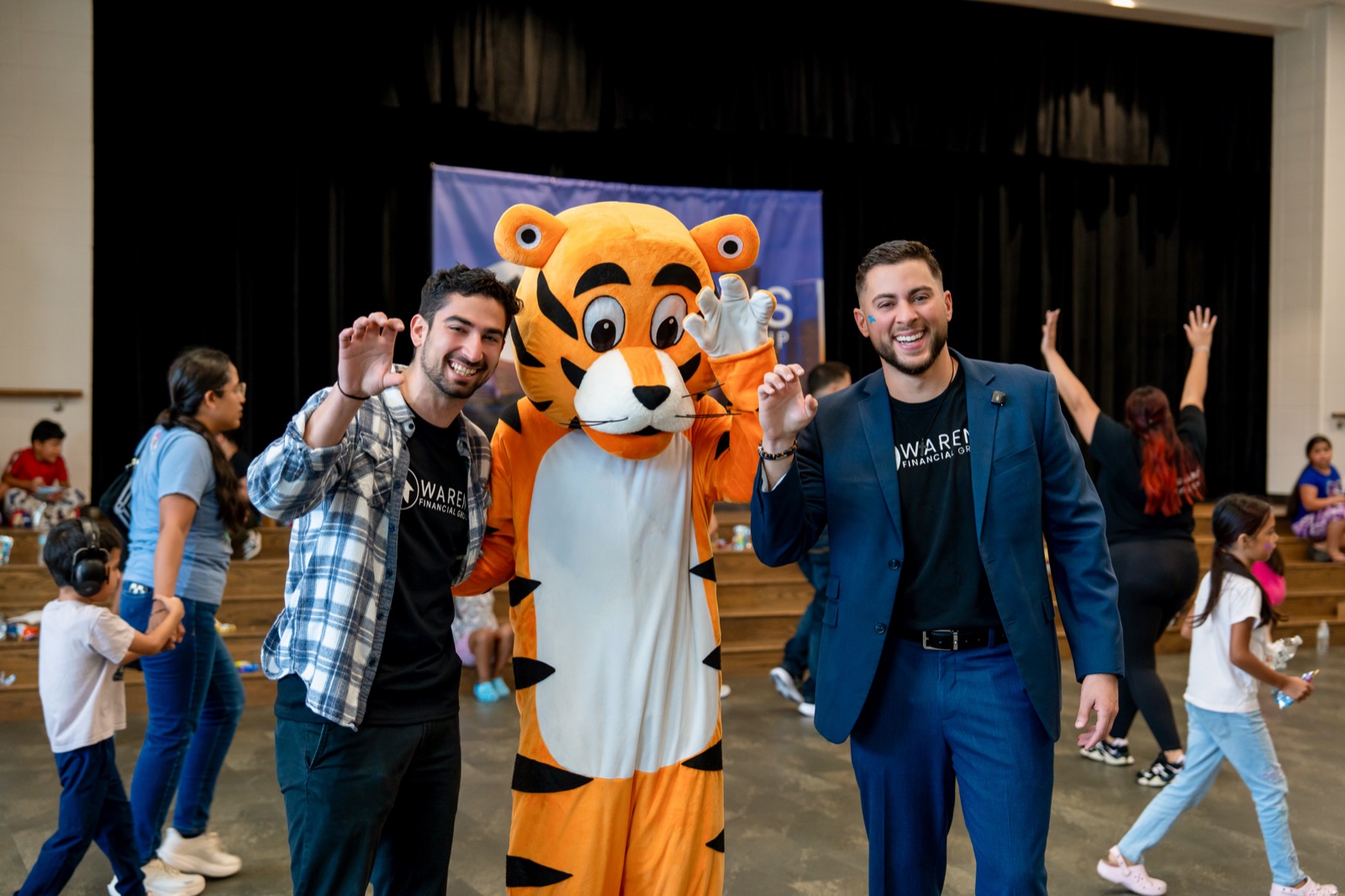 Team members waving beside the tiger mascot