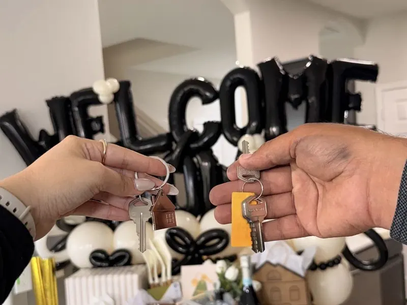 Two hands holding house keys in front of Welcome balloons
